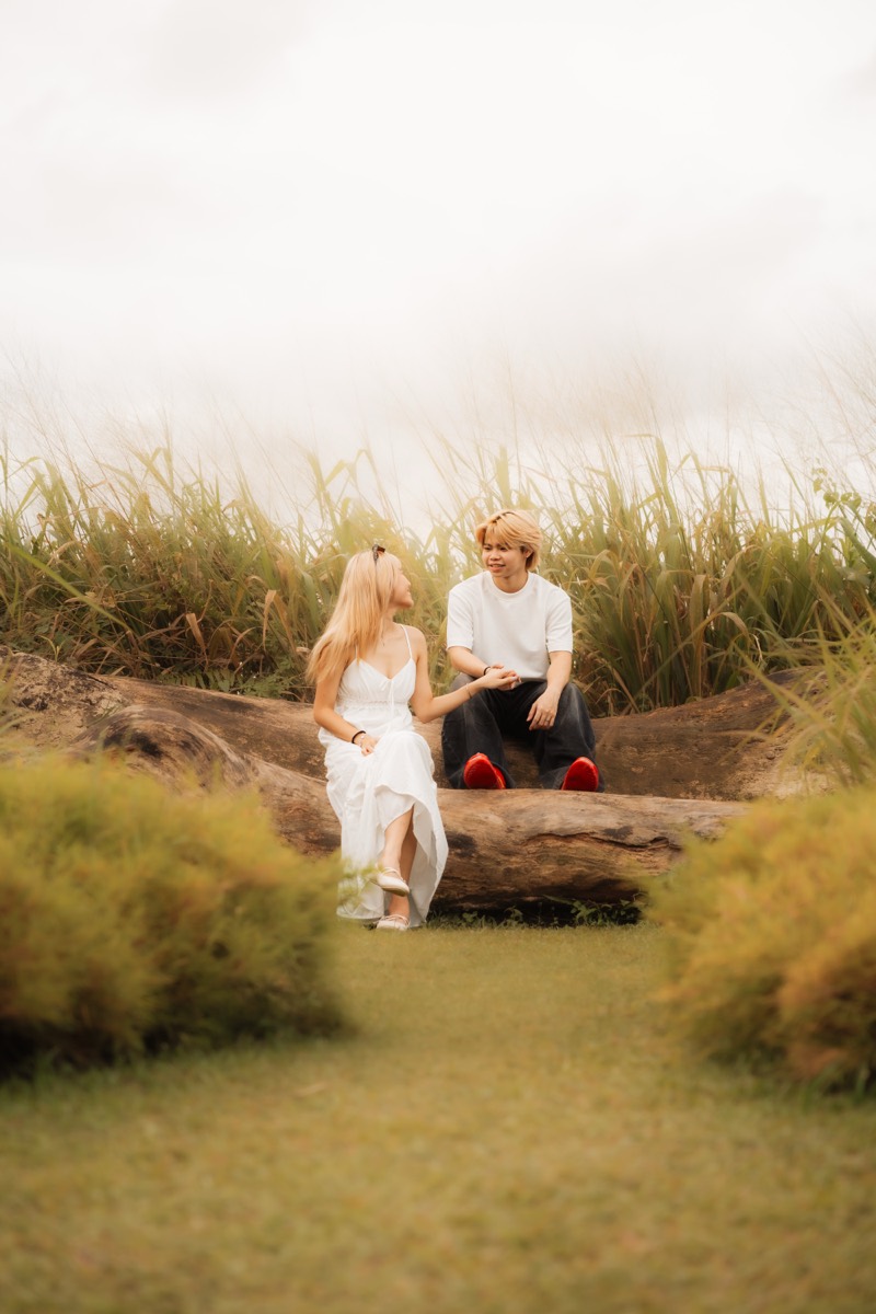 A couple sit close on a fallen log, laughing at something between them.