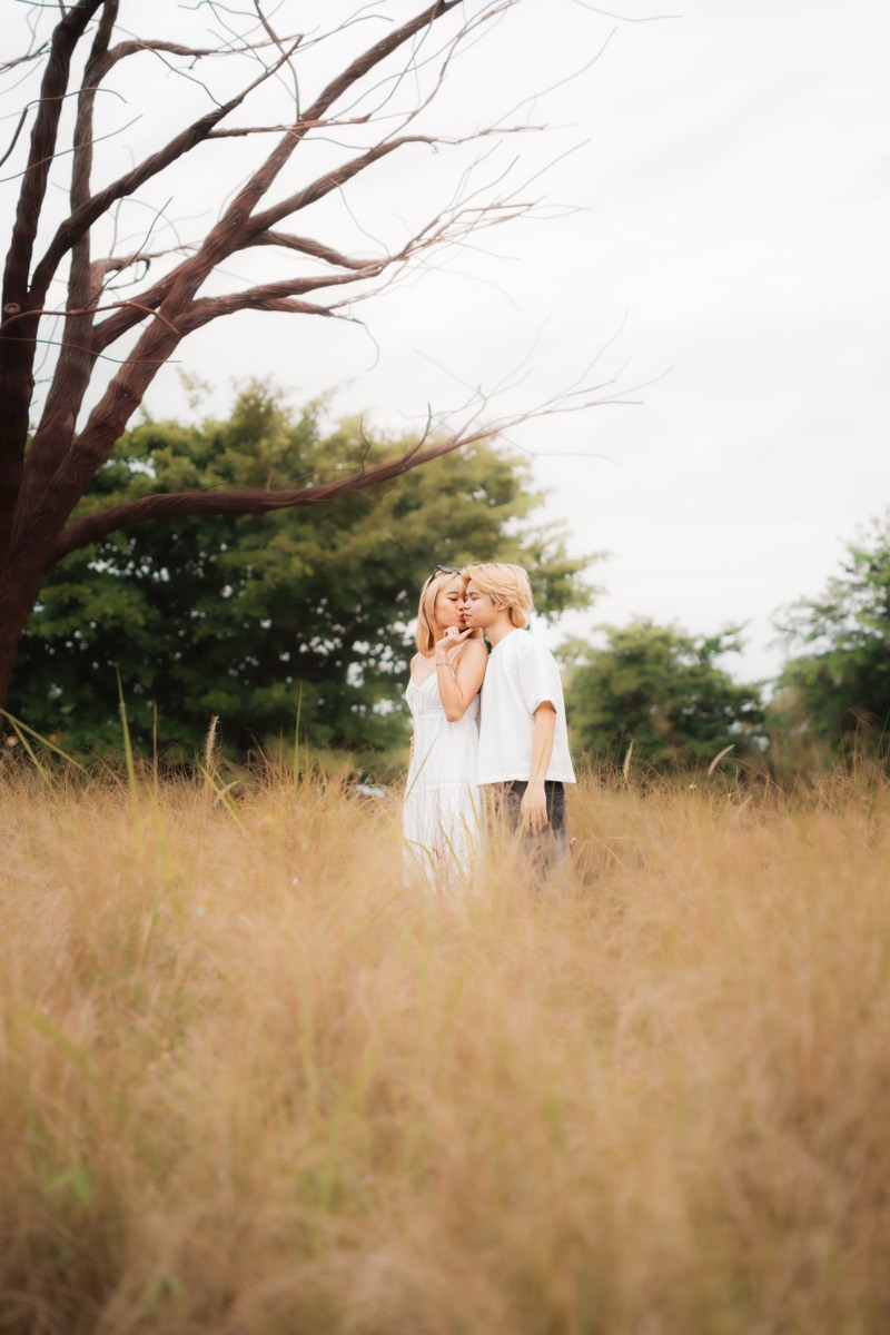 A couple embrace beneath a bare tree in an open field.