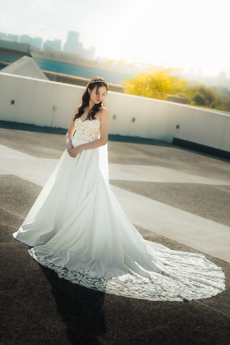 A bride in a long gown on a rooftop, her train fanned out, the skyline behind her.